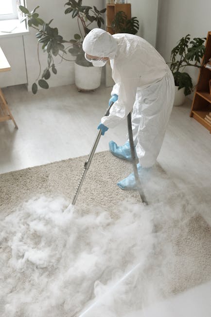 A person vacuuming a patterned, beige and pastel-colored carpet in a room with wooden flooring visible at the edge. The individual, wearing beige shoes and blue jeans, is using a yellow and black vacuum cleaner with a long metal wand to apply surface cleaning and deep cleaning for sanitisation. The scene is well-lit, highlighting the clean condition of the carpet, with the vacuum cleaner's hose connected to the main unit on the floor, situated in a domestic setting. Carpet Cleaning SW6 specializes in professional cleaning services, ensuring hygiene and freshness in residential spaces along Fulham Broadway and New Kings Road.